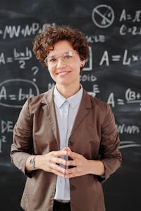 Teacher standing by a blackboard with algebra equations, smiling confidently.